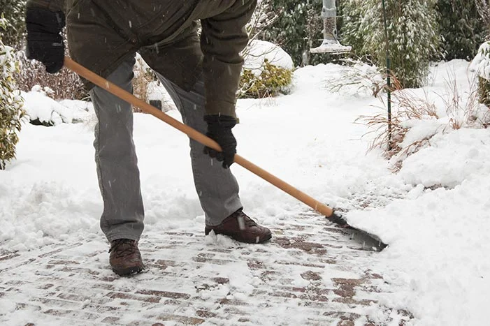 Person räumt Schnee mit Schneeschieber